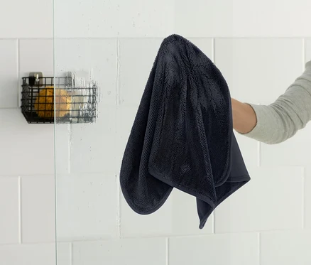 Une personne essuie une cabine de douche avec une serviette bleu foncé.