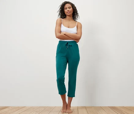 Une femme se tient debout, les bras croisés, portant un pantalon de pyjama vert.
