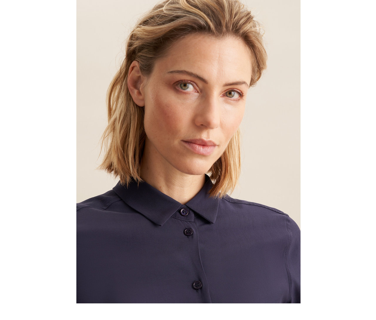 Femme aux cheveux blonds courts portant un chemisier en viscose Seidensticker bleu foncé, regardant l'appareil photo.