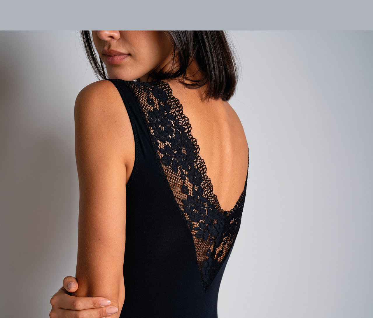 Femme portant un body noir Passionata « Nina » avec un dos en dentelle en V, regardant par-dessus son épaule.
