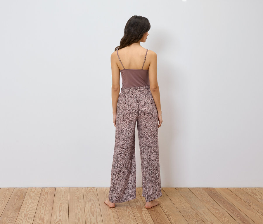 Une femme se tient dos à la caméra, portant un débardeur marron et un pantalon ample à imprimé animalier.