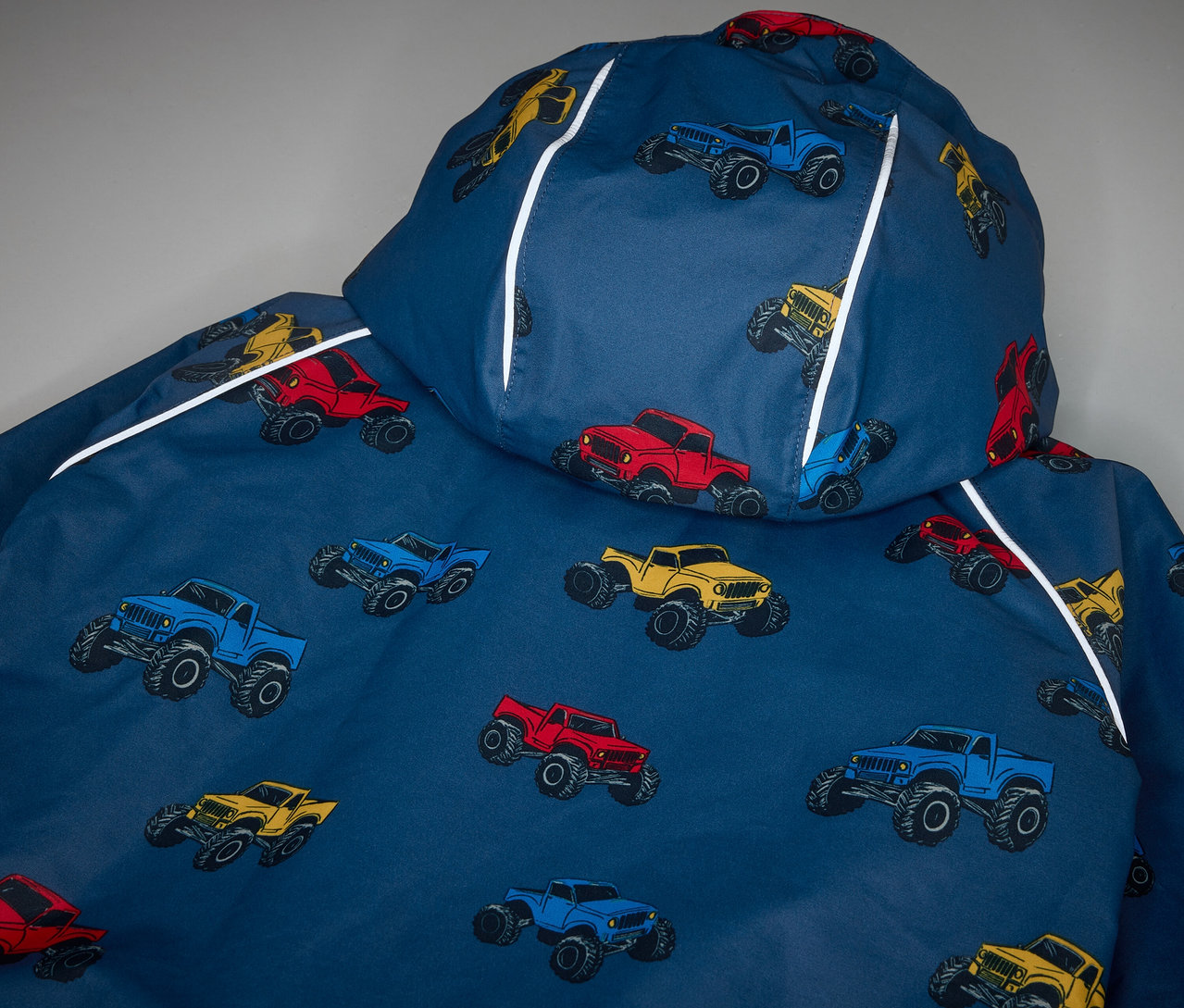 Gros plan sur une veste imperméable thermique pour enfants, imprimée avec des monster trucks.