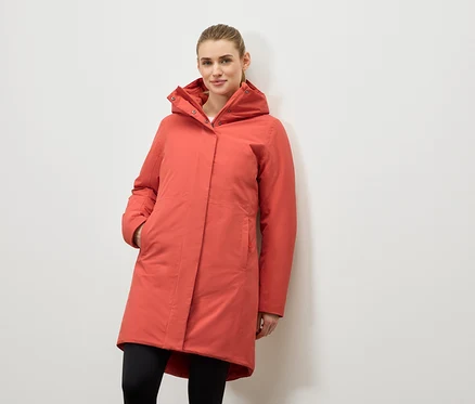 Une femme pose en manteau corail à capuche et leggings noirs.