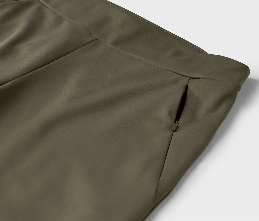 Détail d'un pantalon vert olive avec une poche zippée.