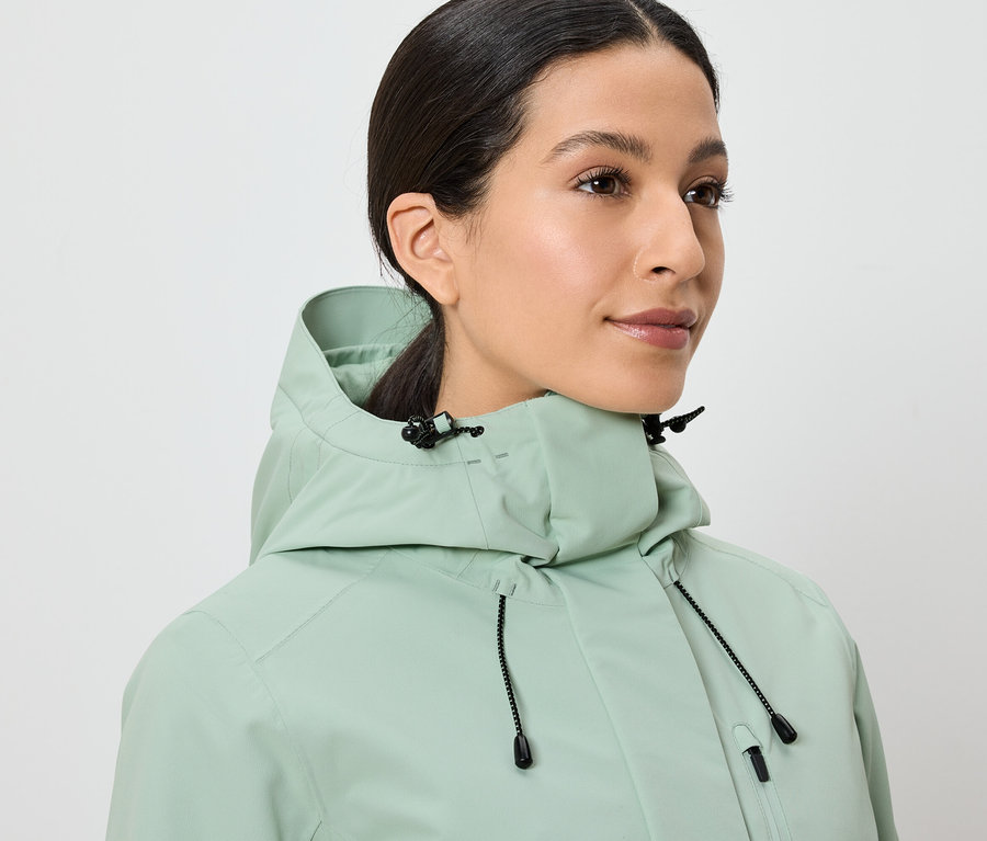 Une femme porte une veste vert clair avec une capuche.