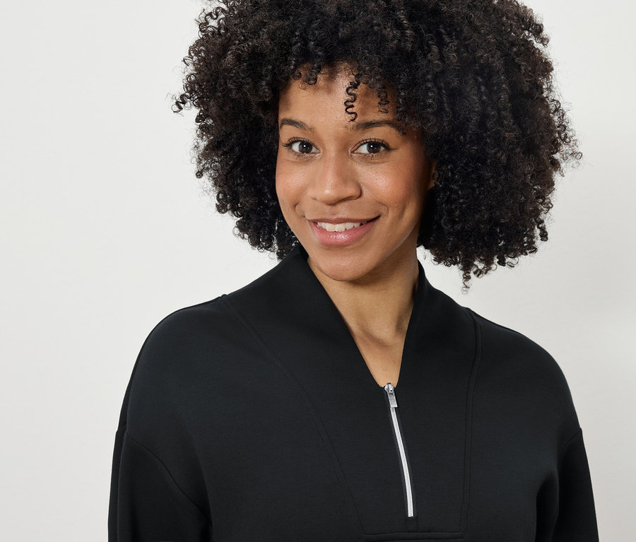 Portrait d'une femme souriante avec une coiffure afro dans un sweat-shirt noir zippé.