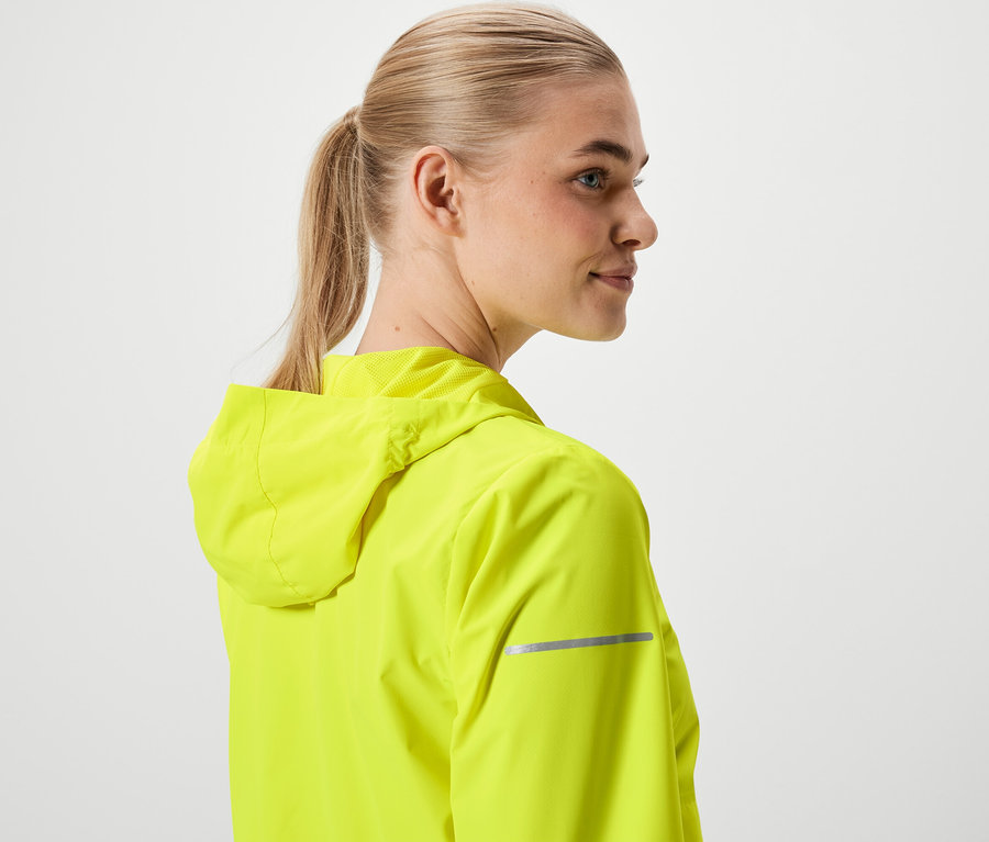 Femme blonde aux cheveux attachés en queue de cheval, portant une veste jaune néon à capuche.