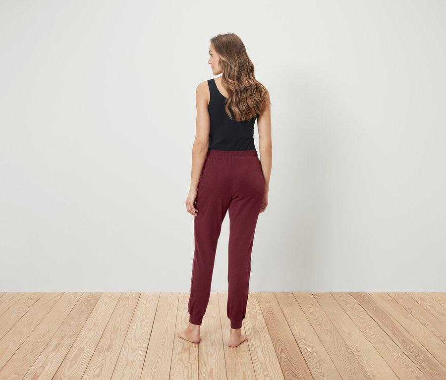 Une femme se tient dos à l'appareil photo, portant un débardeur noir et un pantalon de survêtement bordeaux.