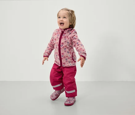Bambin portant une veste en polaire rose à fleurs et un pantalon rose.