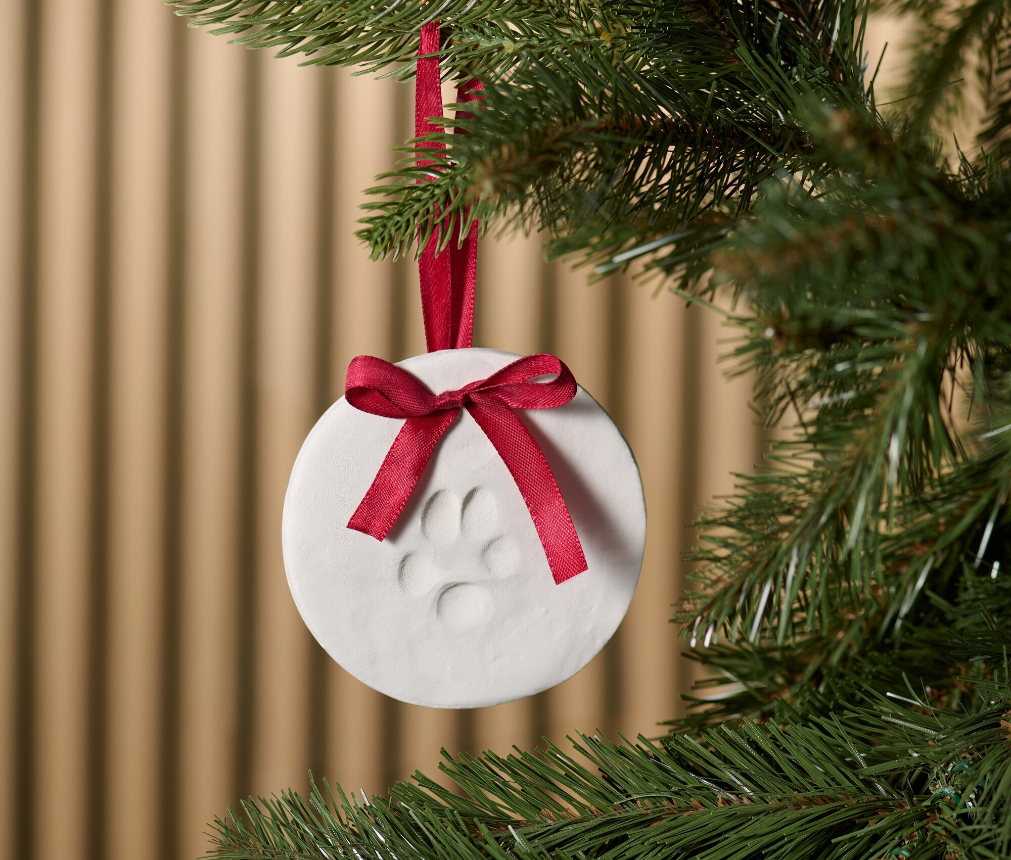 Un ornement blanc avec une empreinte de patte et un ruban rouge suspendu à un arbre de Noël.