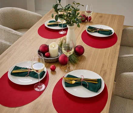 Table dressée avec quatre couverts comprenant des sets de table rouges, des assiettes blanches, des serviettes vertes et des couverts dorés.