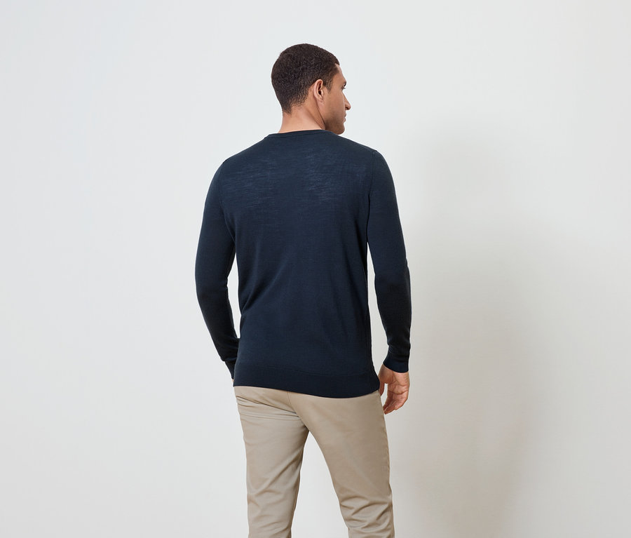 Un homme vu de dos, vêtu d'un pull bleu marine et d'un pantalon beige.