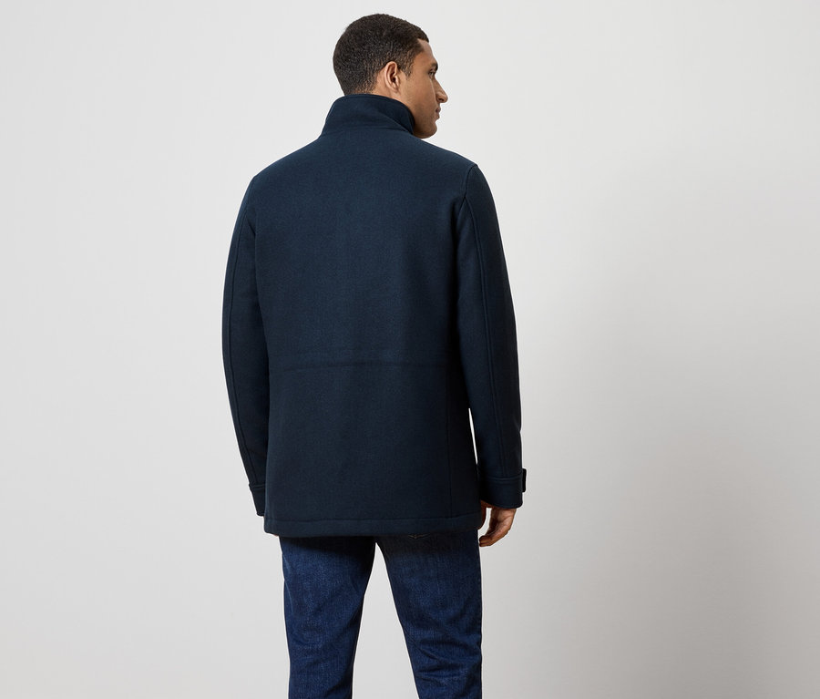 Homme vu de dos portant un manteau bleu marine et un jean.