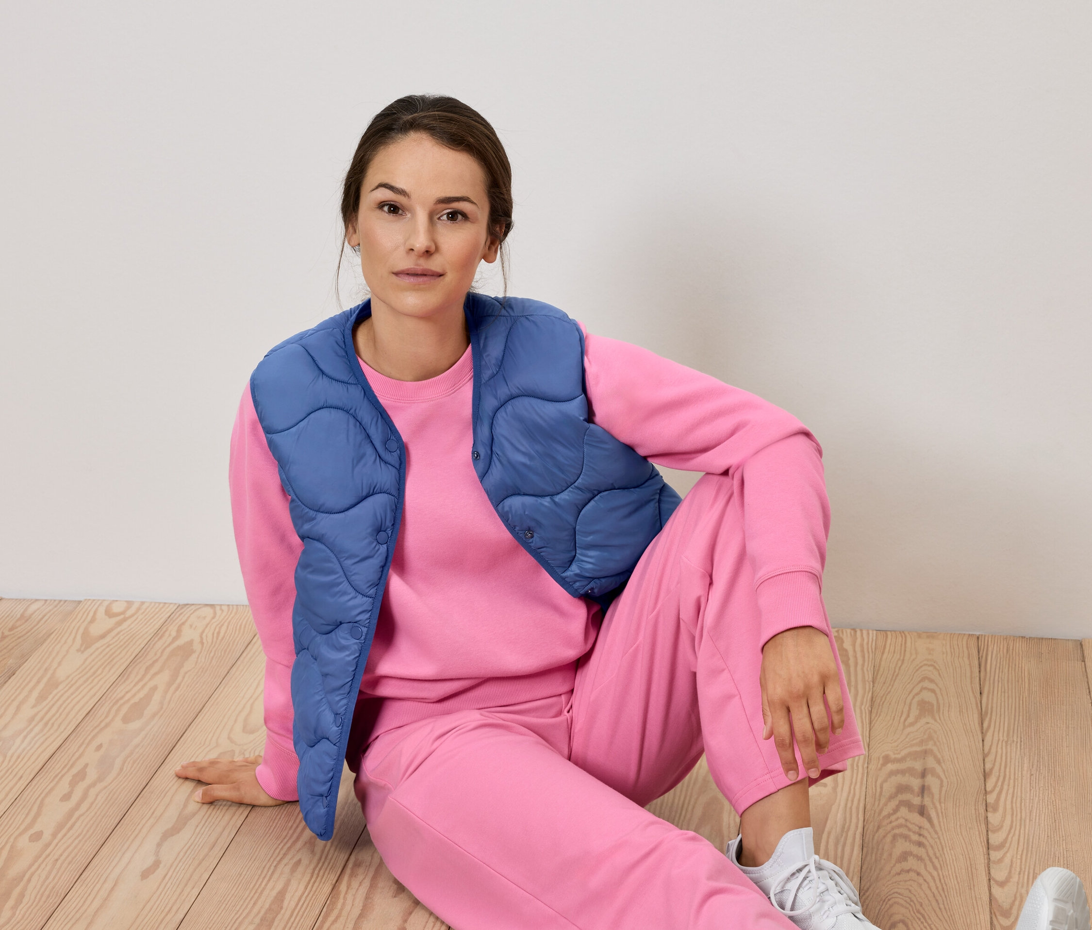 Femme assise par terre en survêtement rose et gilet bleu.