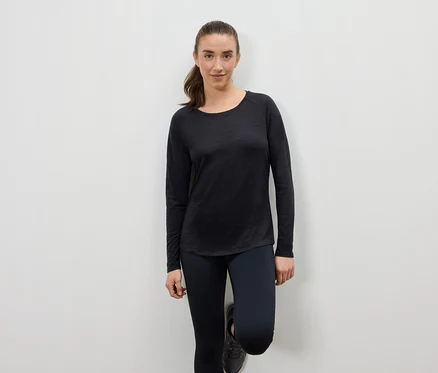 Femme en vêtements de sport noirs appuyée contre un mur.