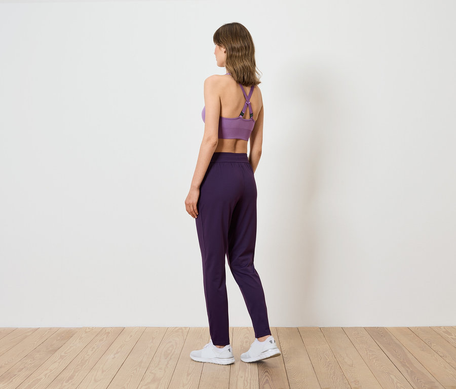 Une femme vue de dos portant un soutien-gorge de sport violet et un pantalon violet foncé.