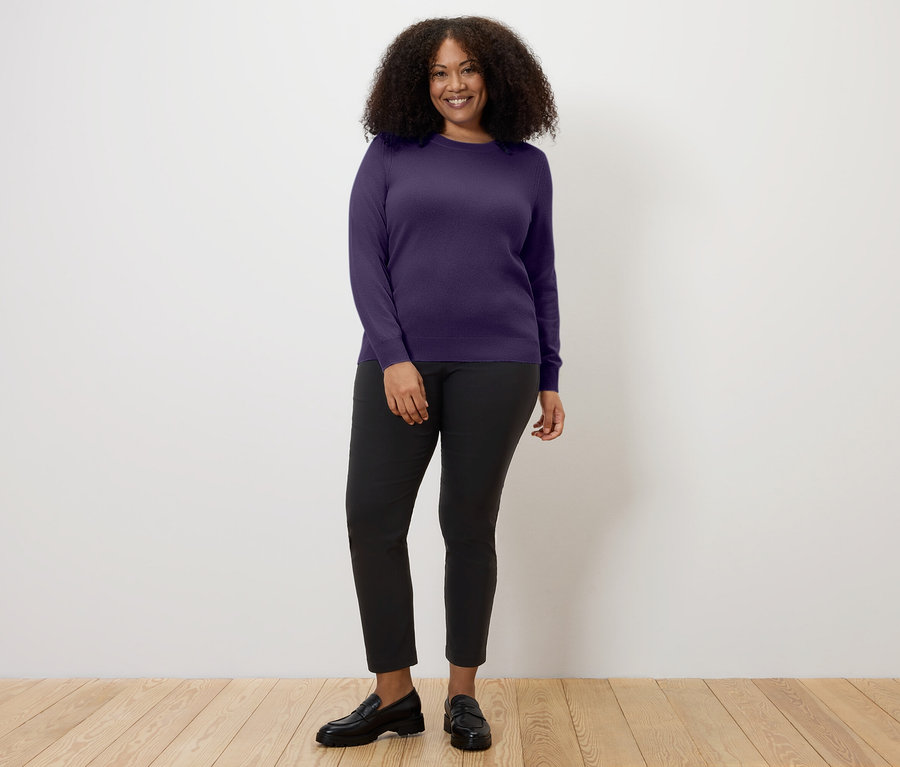 Une femme portant un pull en maille fine avec du cachemire prune, un pantalon noir et des mocassins noirs.