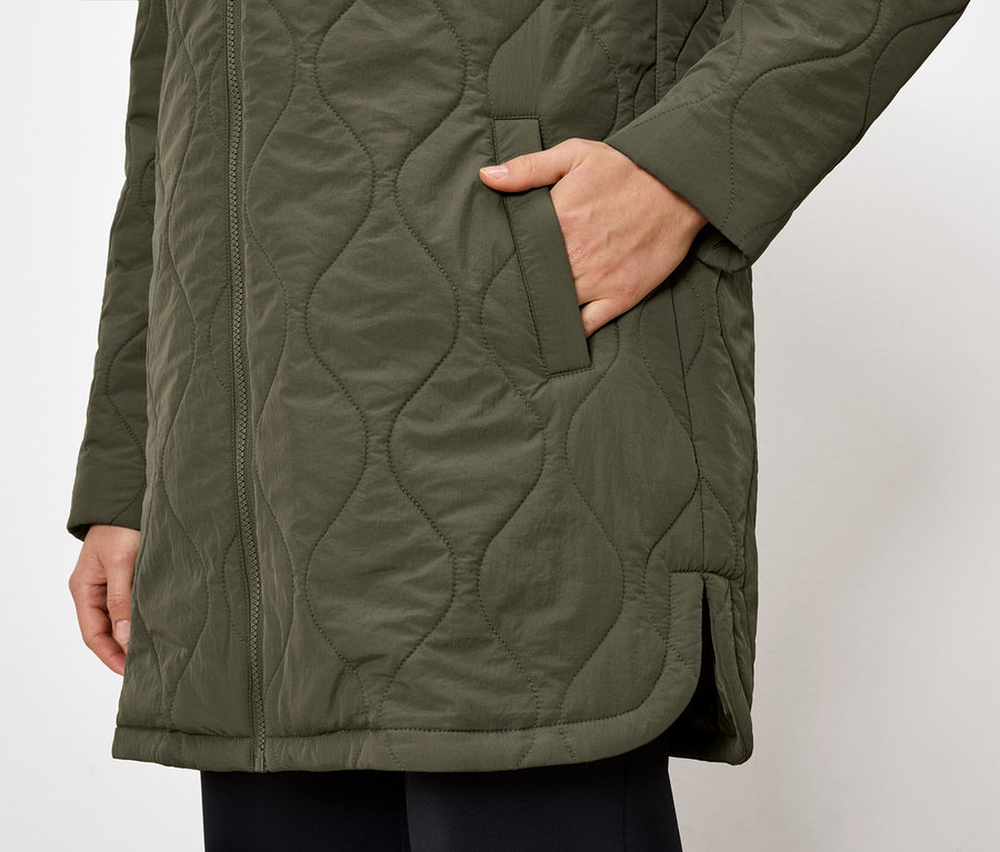 Gros plan sur une veste matelassée vert olive avec une main dans la poche.