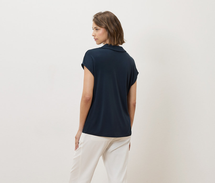Une femme regarde par-dessus son épaule et porte un t-shirt bleu marine et un pantalon blanc.