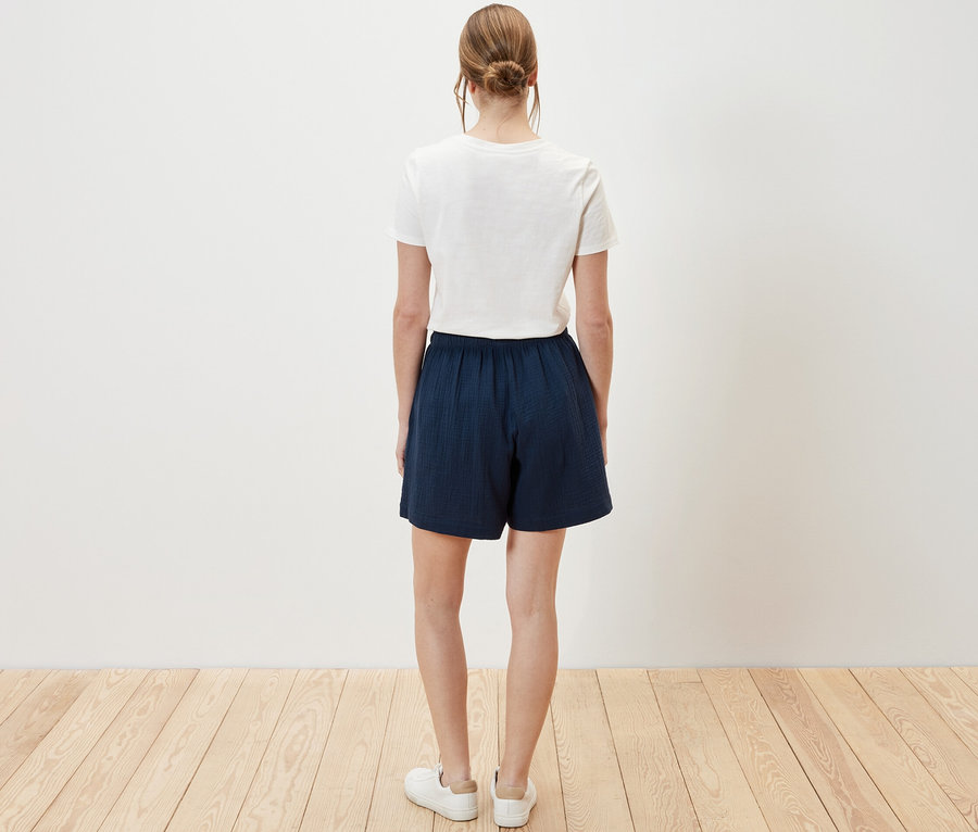 Femme vue de dos portant un short en mousseline et un t-shirt blanc.