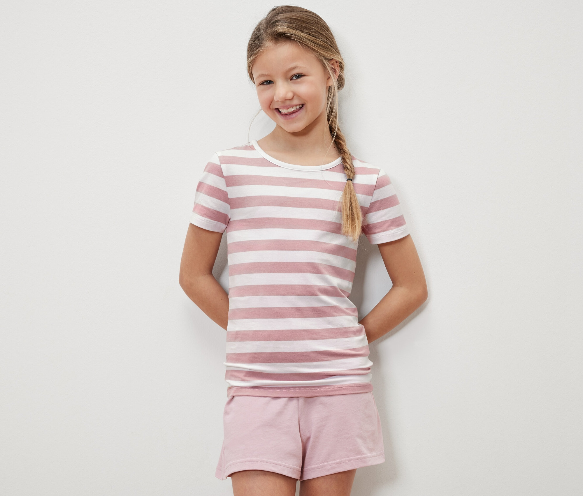 Fillette souriante posant dans un t-shirt enfant rayé rose et blanc et un short rose.