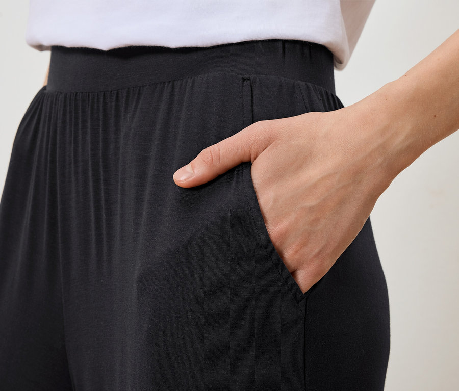 Femme mettant la main dans la poche d'un pantalon noir.