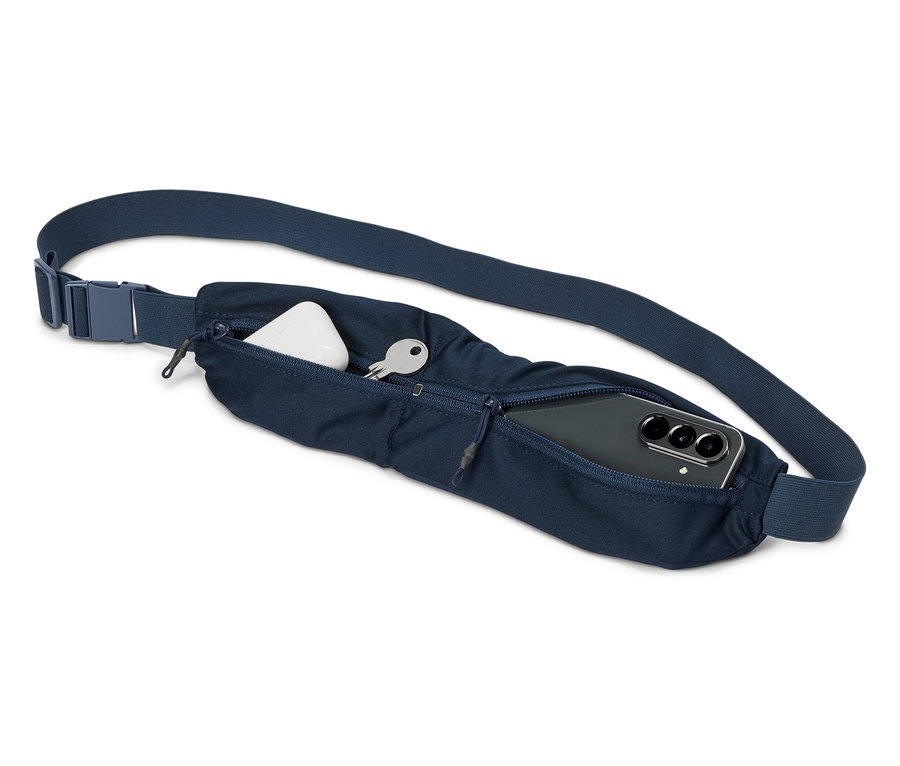 Gros plan d'un sac banane bleu marine avec une clé, des écouteurs et un smartphone dans les compartiments.