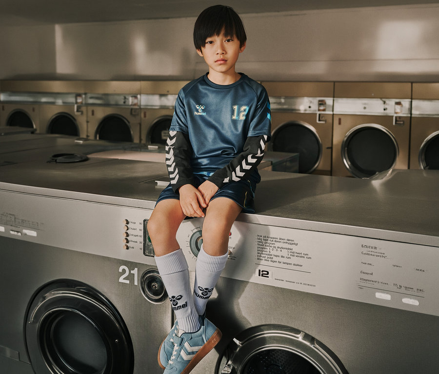 Garçon portant l'ensemble maillot hummel® pour enfant HMLSHIMMER bleu marine assis sur une machine à laver.