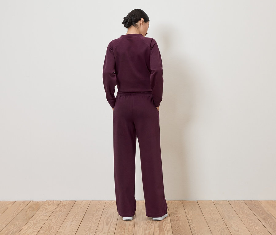 Vue de dos d'une femme aux cheveux relevés, portant une tenue de sport bordeaux composée d'un haut et d'un pantalon.