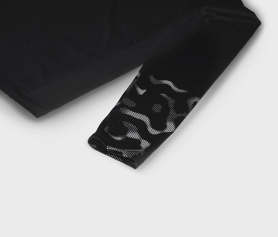 T-shirt noir à manches longues avec motif à pois blancs à l'extrémité de la manche, posé sur un fond blanc.