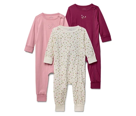 Trois pyjamas pour bébés sont alignés : un rose, un blanc à motifs floraux et un bordeaux.