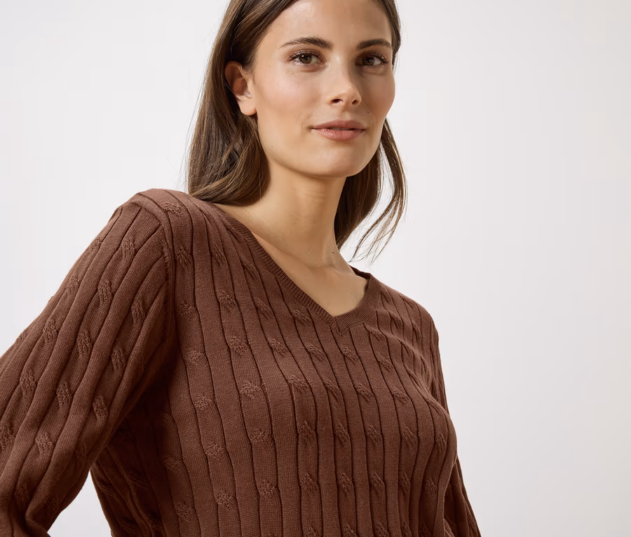 Une femme aux longs cheveux bruns porte un pull marron à col en V.