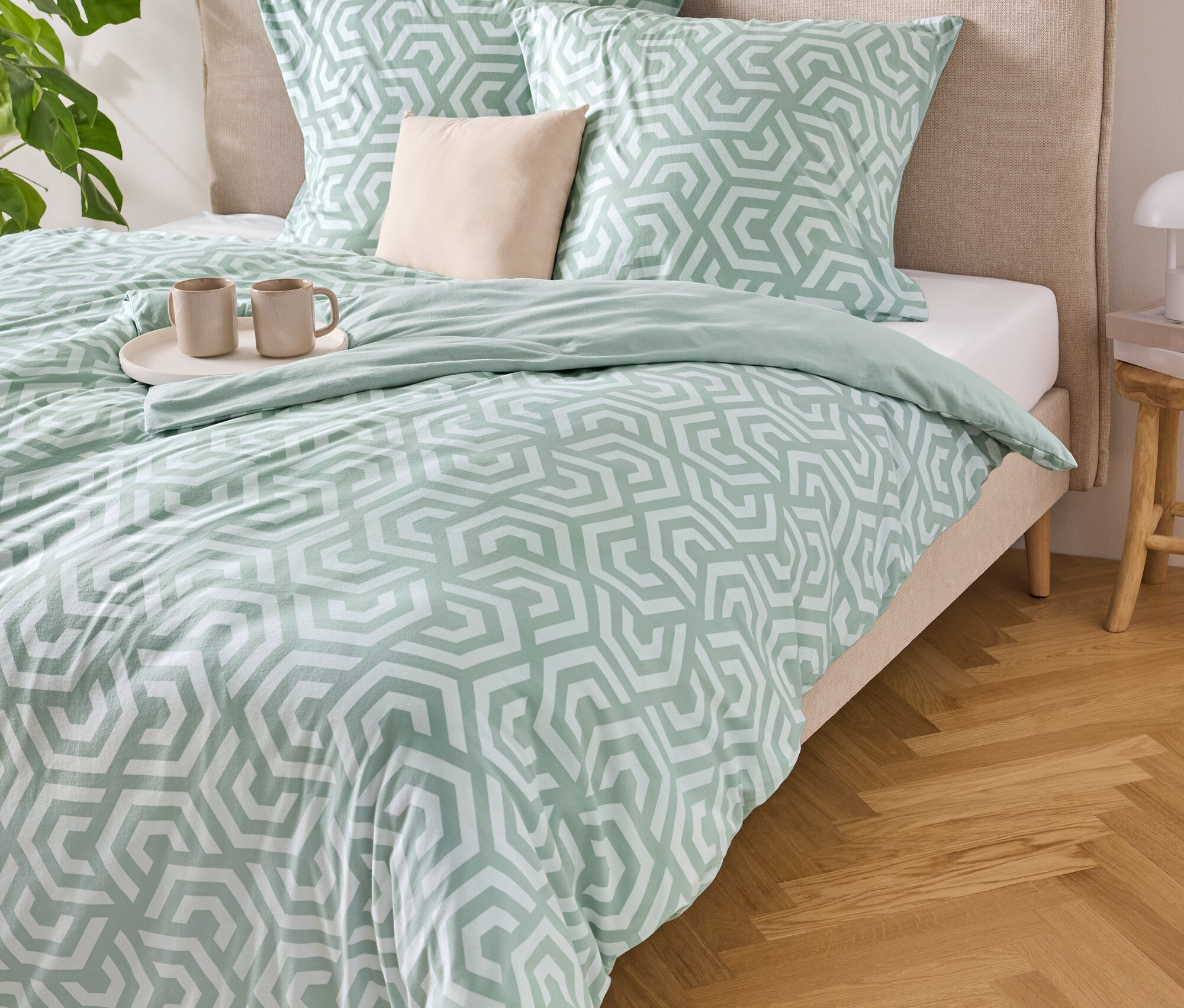 Un lit avec des draps rayés bleu clair et blanc, deux oreillers et un plateau avec deux tasses dessus.