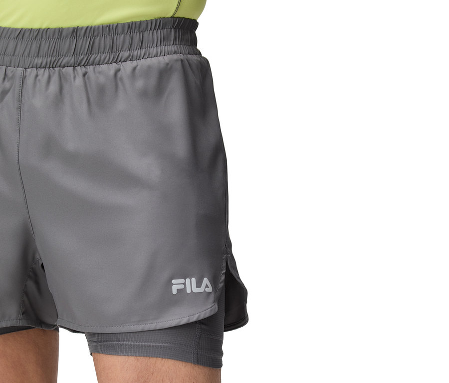 Gros plan d'une personne portant un short Fila gris avec cordon de serrage et logo Fila.