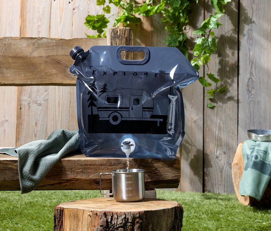 De l'eau est versée d'une poche à eau grise avec un motif de caravane dans une tasse posée sur une souche d'arbre.