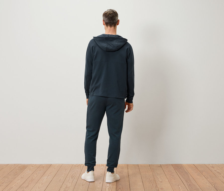 Vue arrière d'un homme aux cheveux gris portant un sweat à capuche bleu marine, un pantalon de jogging et des baskets blanches.