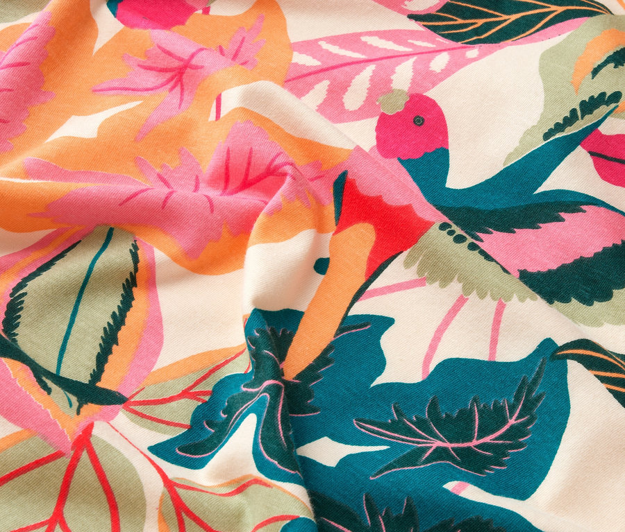 Gros plan d'un tissu à motifs de feuilles et d'oiseaux en rose, orange, vert et bleu sur fond beige.