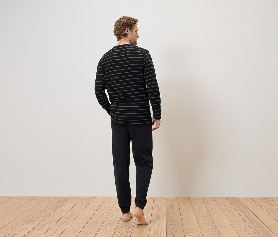 Un homme se tient pieds nus, de dos, vêtu d'un haut rayé à manches longues et d'un pantalon noir.