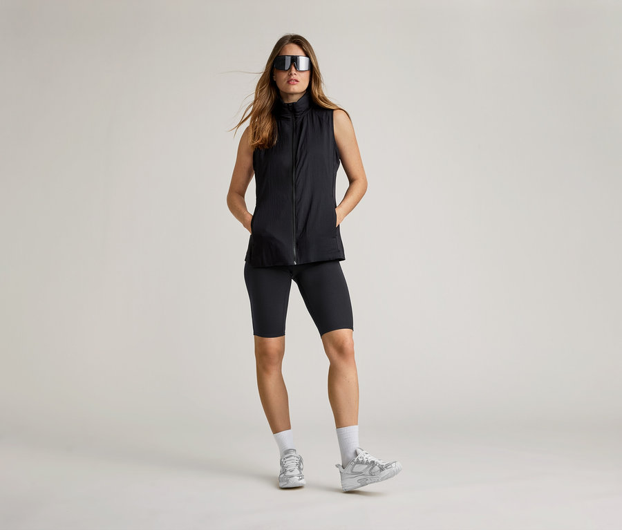 Femme portant des lunettes de soleil et un gilet de course noir. Elle porte un cycliste, des chaussettes et des baskets.