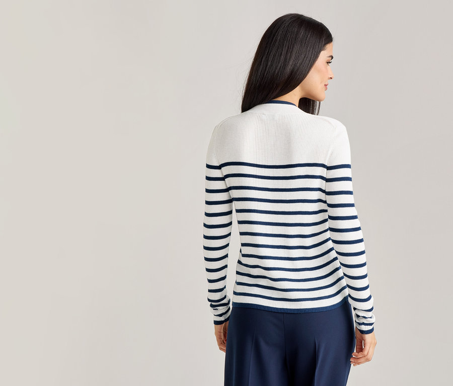 Une femme vue de dos, aux cheveux foncés, porte un pull rayé blanc et bleu marine et un pantalon bleu marine.