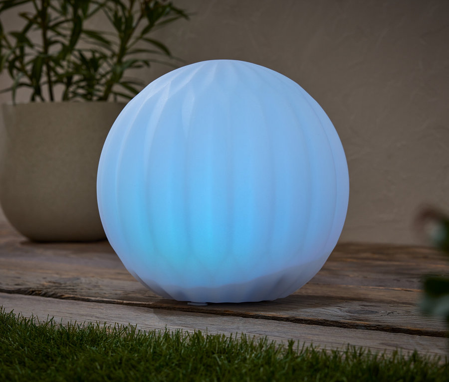 Une sphère bleue brille sur une surface en bois, à côté d'une plante en pot.