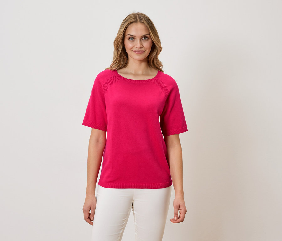 Femme portant un t-shirt rose et un pantalon blanc.