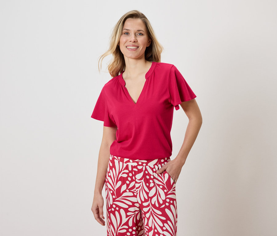 Une femme porte un t-shirt rouge et un pantalon blanc avec un motif rouge.