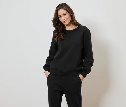 Une femme portant un sweat-shirt et un pantalon noirs pose devant un fond blanc.