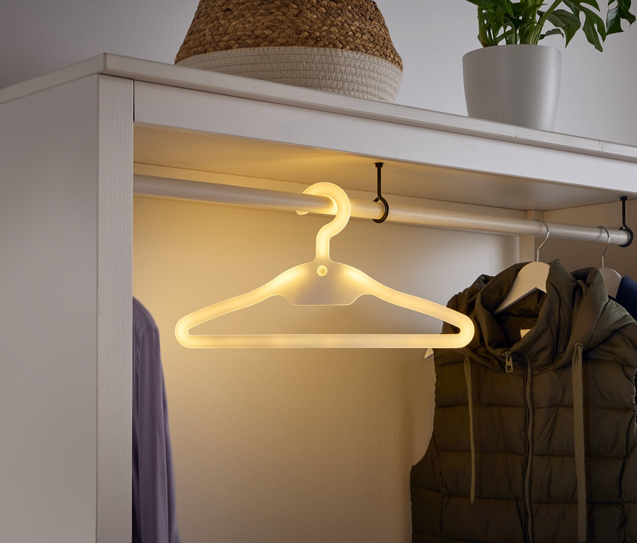 Dans une armoire blanche, un cintre lumineux est suspendu à une barre, à côté d'un gilet et d'une chemise.