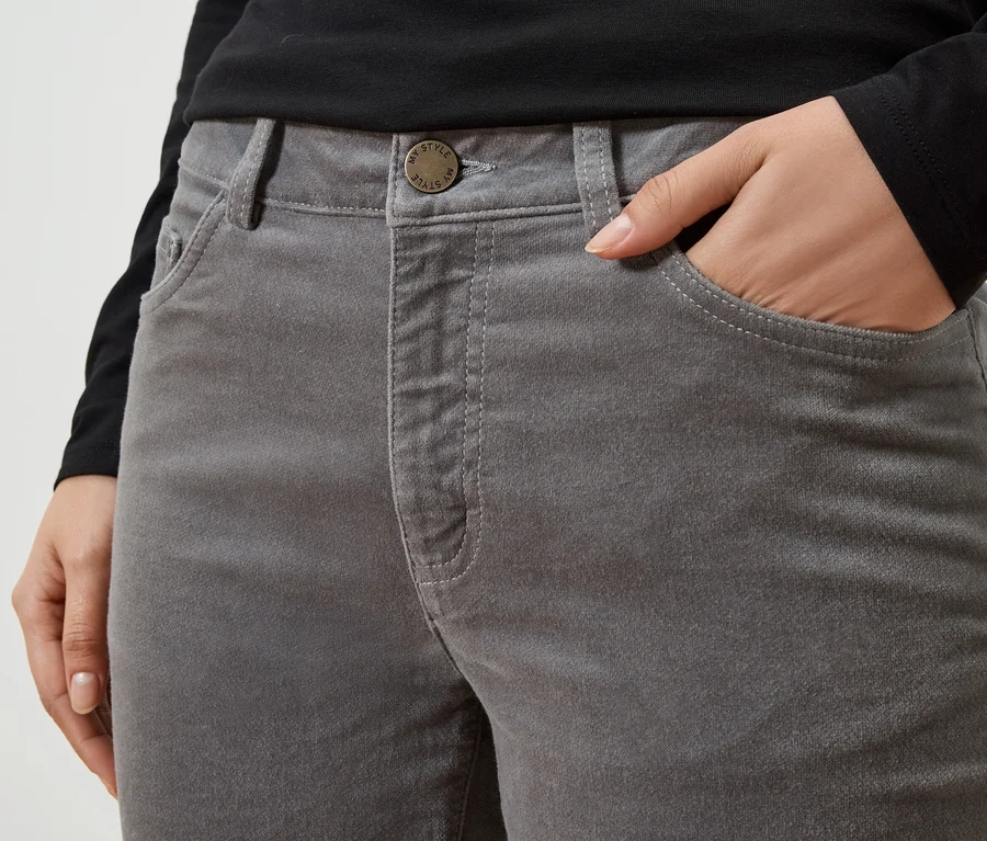 Gros plan d'une personne avec une main dans la poche d'un pantalon gris. La personne porte un haut noir.