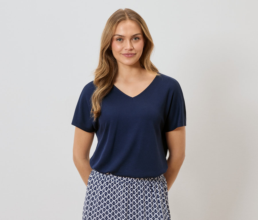 Femme aux cheveux blonds portant un T-shirt bleu marine et une jupe à motifs bleus et blancs.