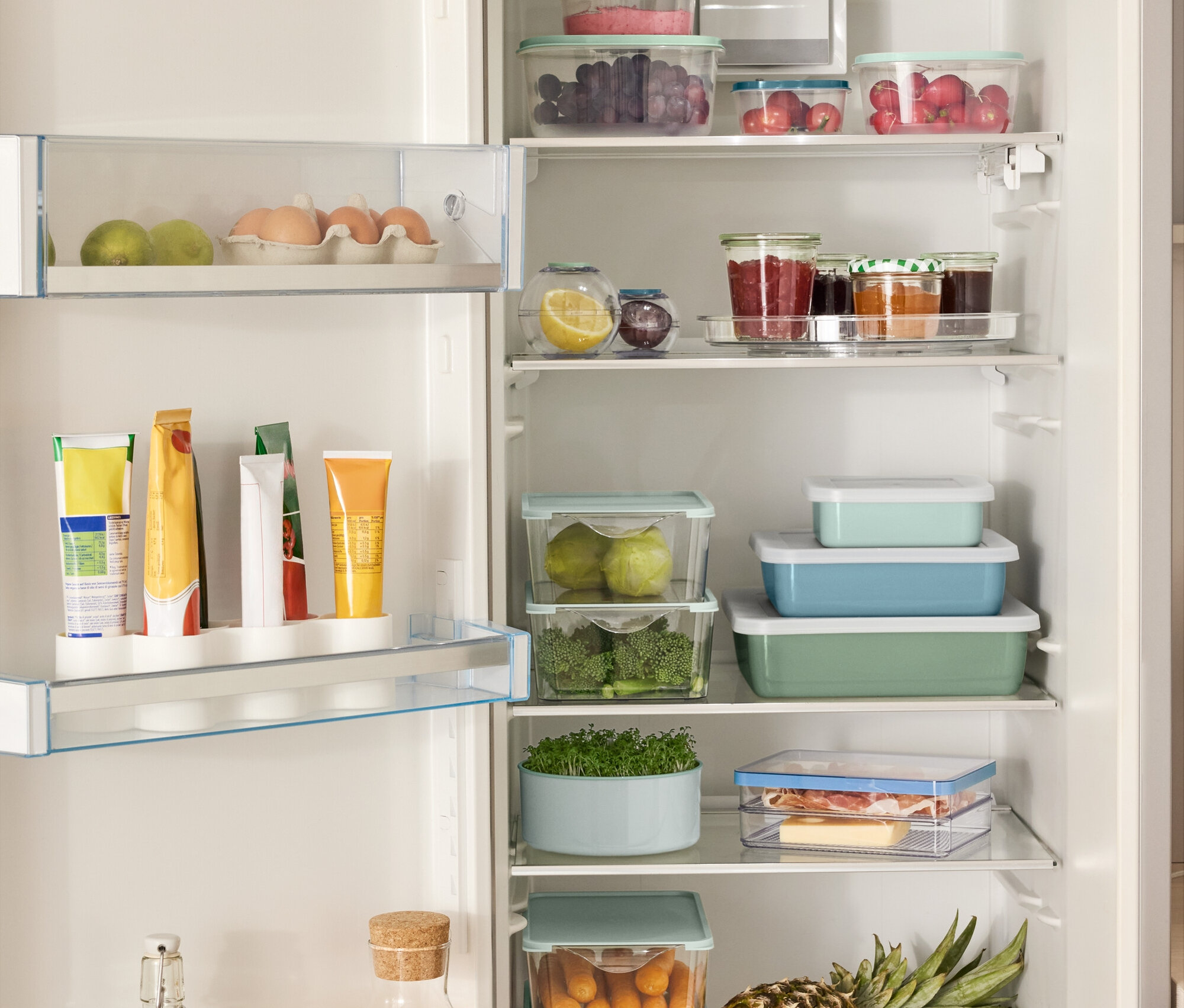 Réfrigérateur ouvert rempli de divers aliments, dont 4 boîtes de rangement, 2 boîtes fraîcheur en forme de boule, 3 plats de cuisson émaillés avec couvercle et un plateau tournant.