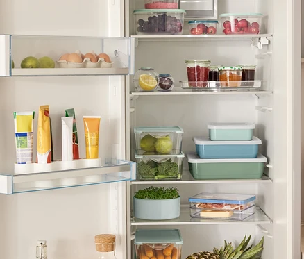 Réfrigérateur ouvert rempli de divers aliments, dont 4 boîtes de rangement, 2 boîtes fraîcheur en forme de boule, 3 plats de cuisson émaillés avec couvercle et un plateau tournant.