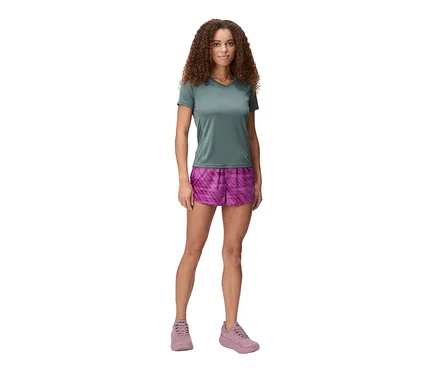 Femme debout sur fond blanc portant un t-shirt vert, un short rose et des chaussures roses.